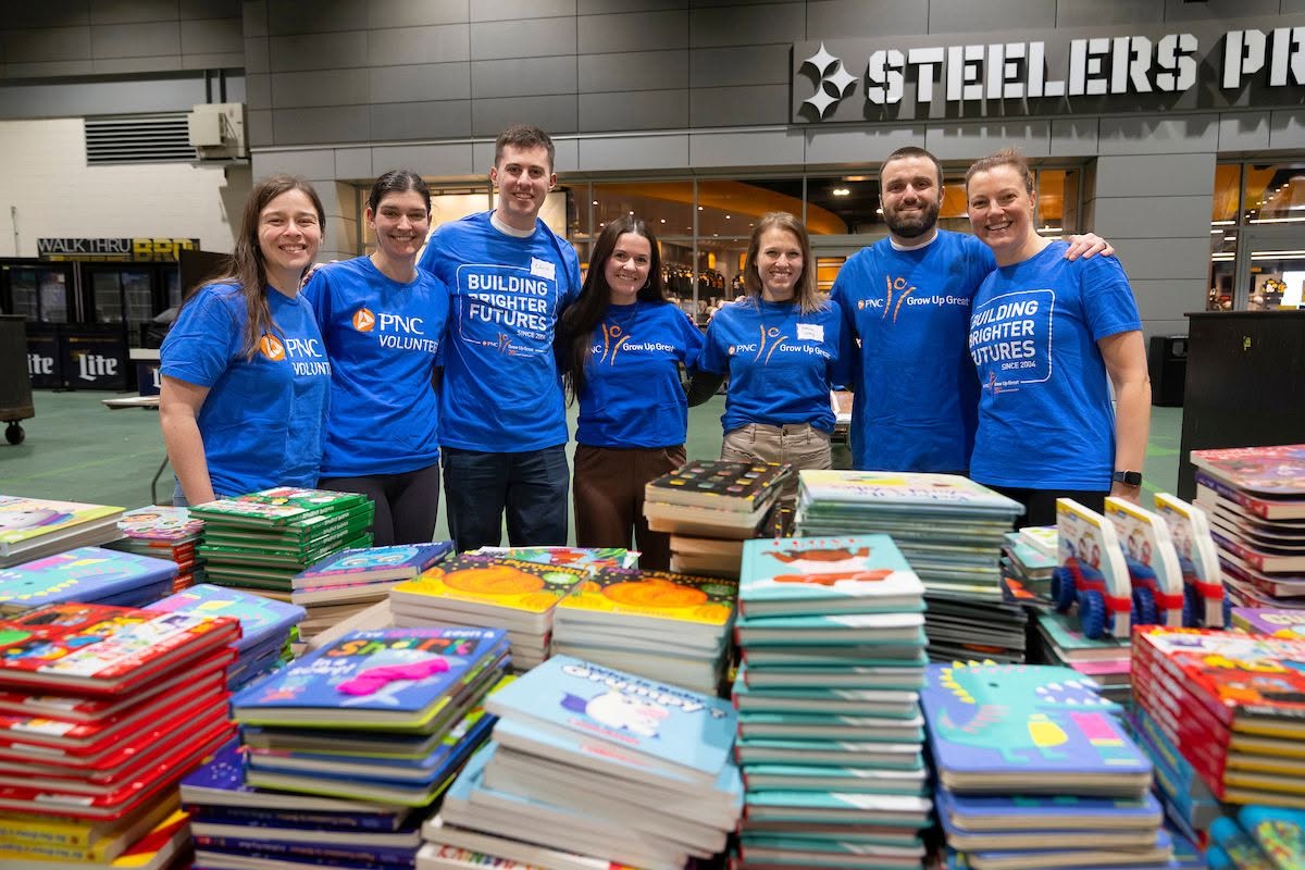 A group of young adults wearing blue shirts behind a table of books.