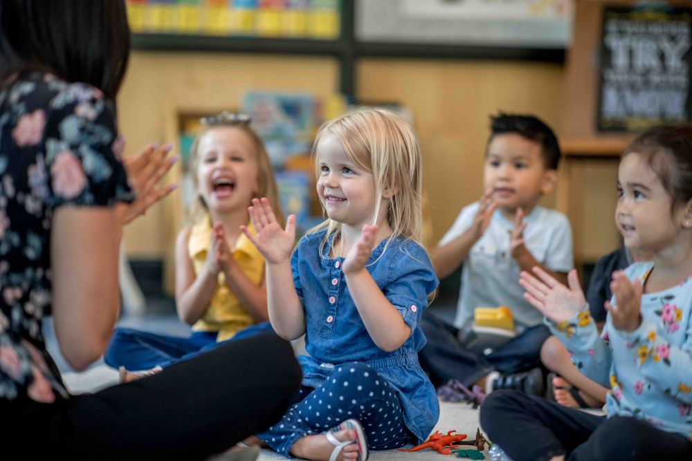 A group of young children sitting on the floor clapping.