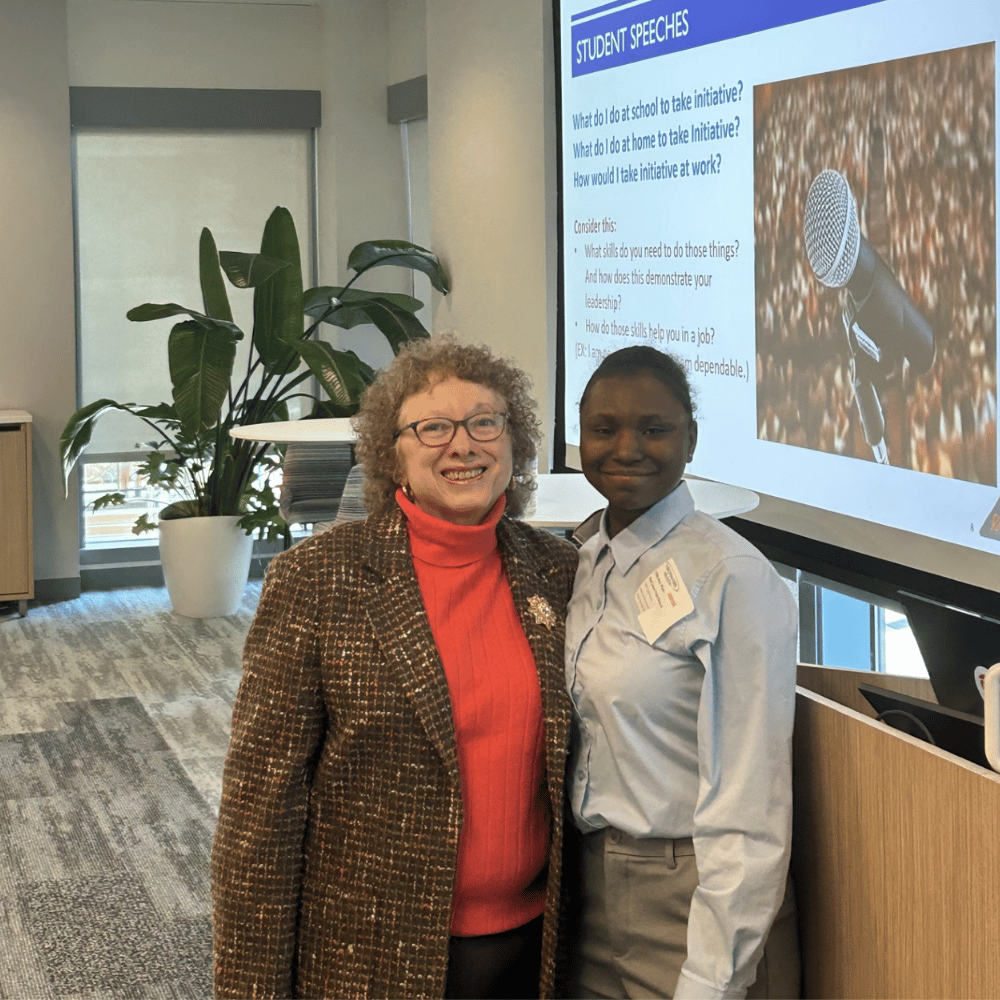 Two women standing in front of a presentation screen with plants in the background